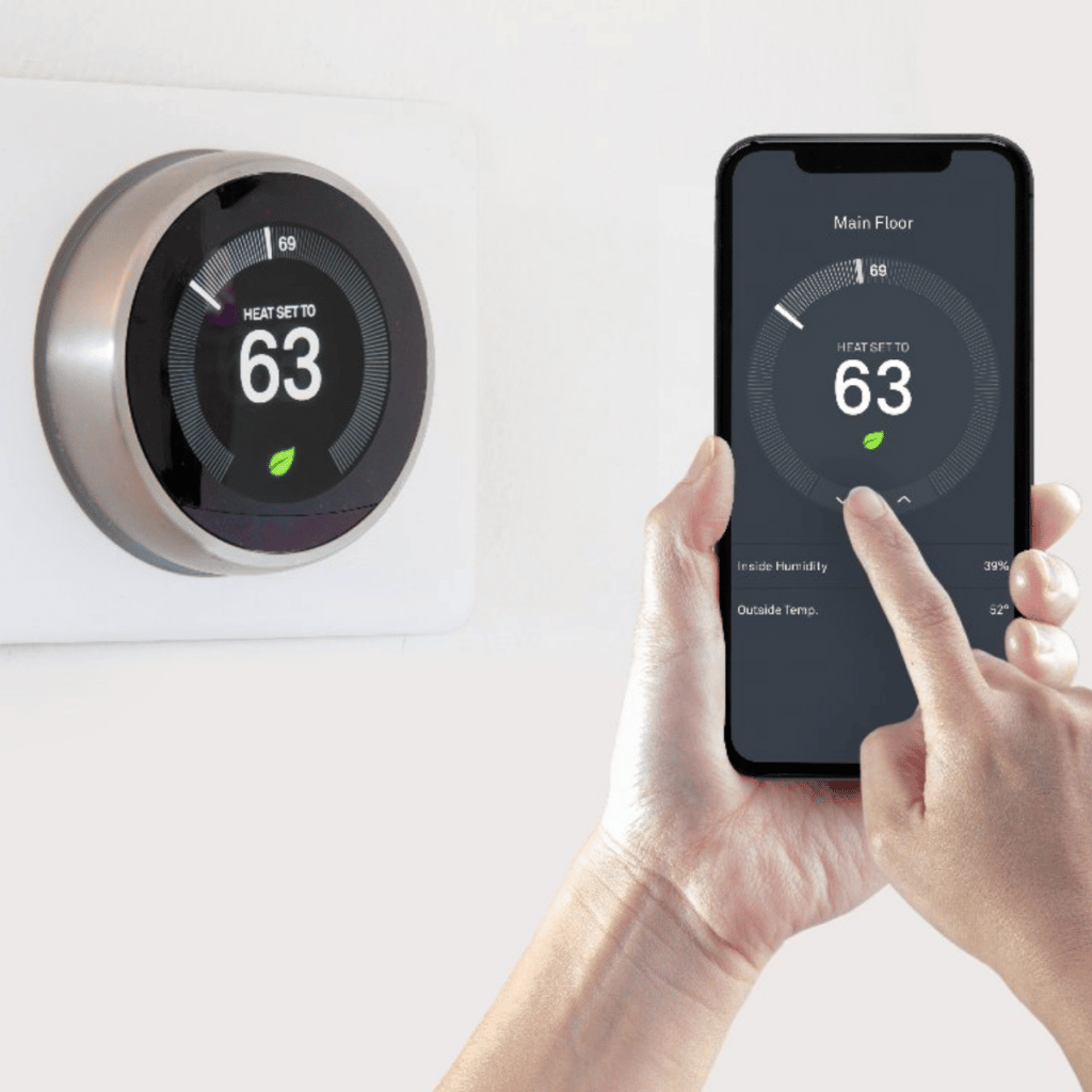 hand holding smart phone adjusting smart thermostat temperature with smart thermostat installed on the wall in the background