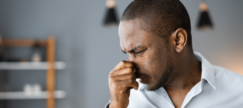 man plugging his nose due to bad smell coming from heater inside home